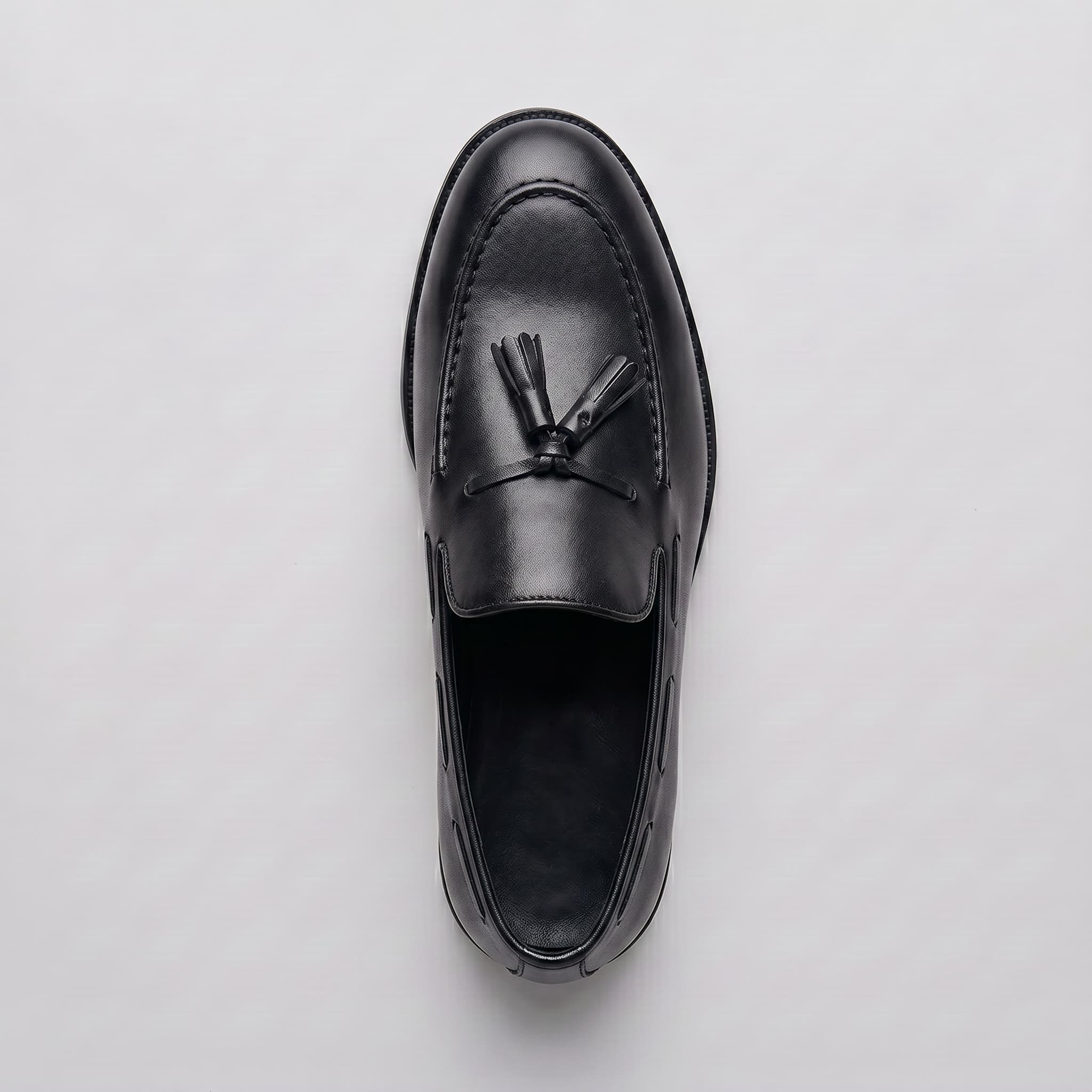 Black leather loafer with tassel on a light gray background