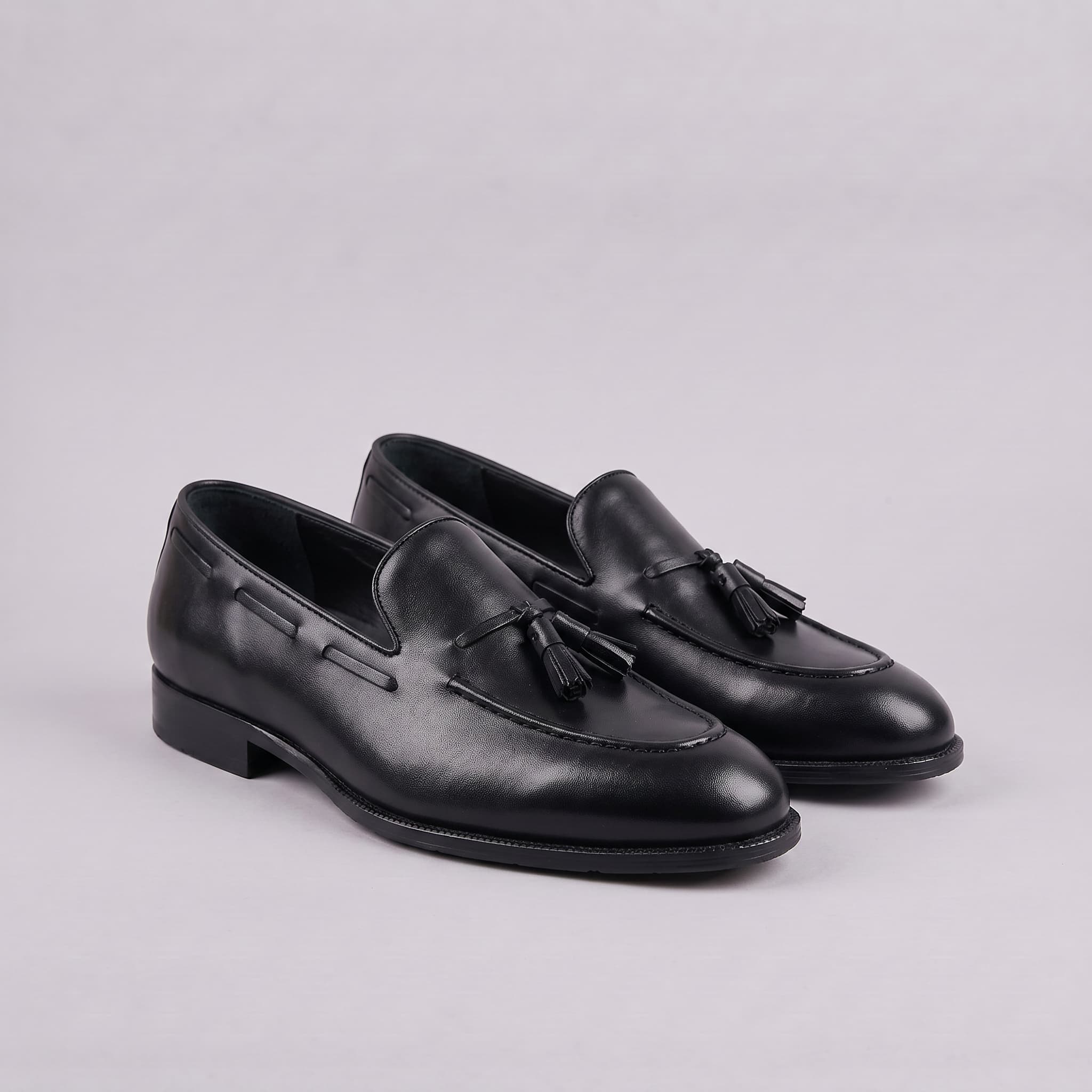 Pair of black loafers with tassels on a light gray background