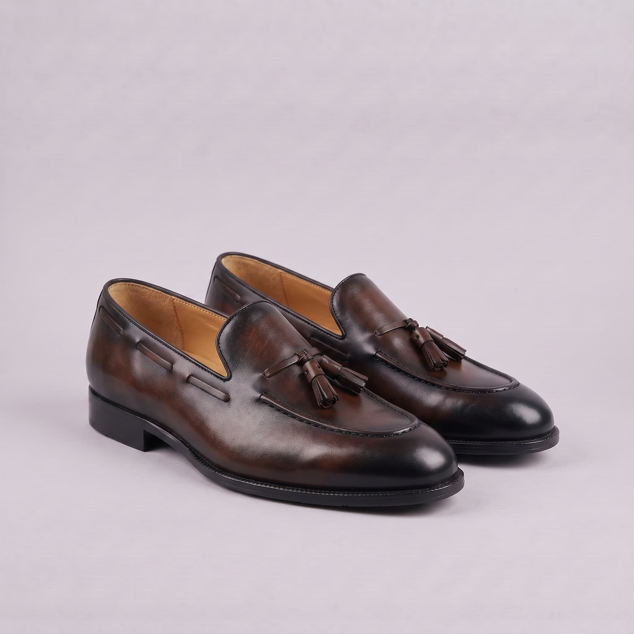 Pair of brown leather loafers with tassels on a light gray background