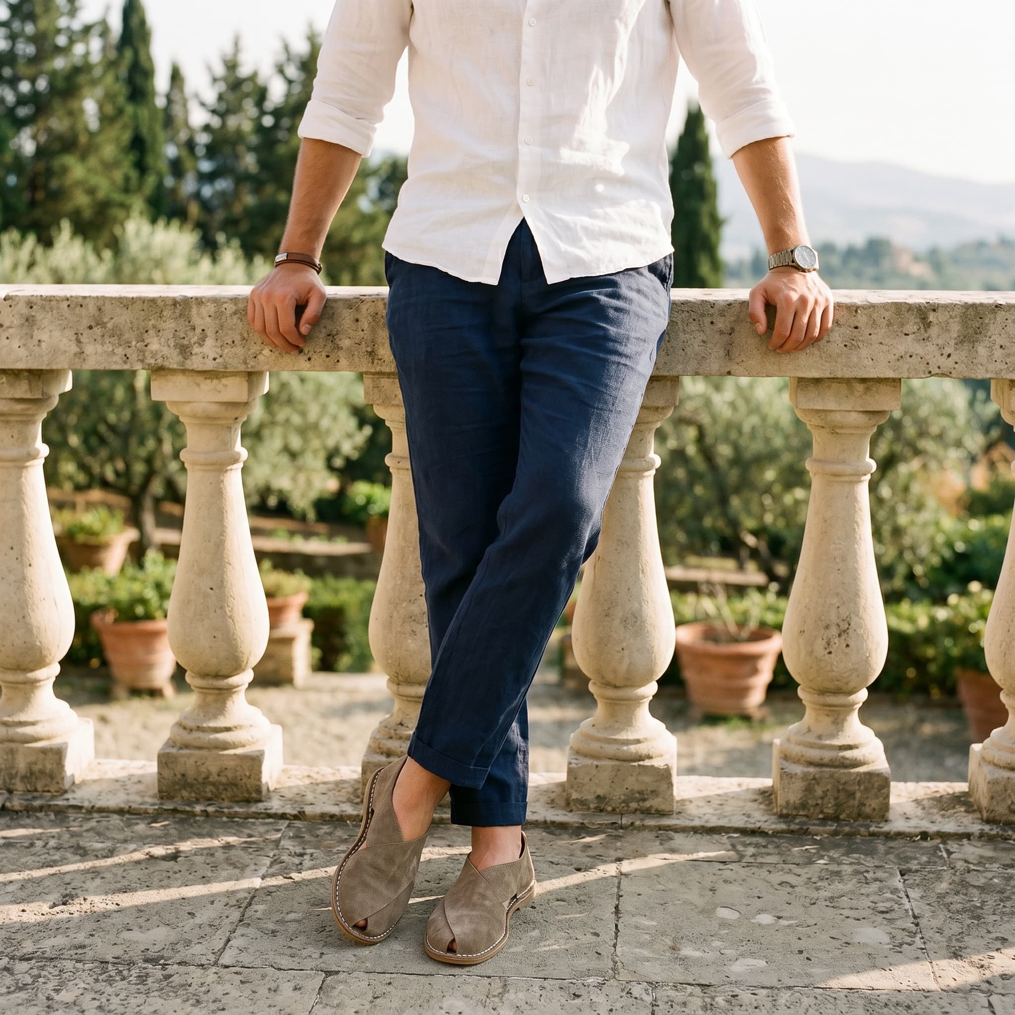 Person wearing a white shirt, blue pants, and brown shoes standing on a stone path with greenery in the background.