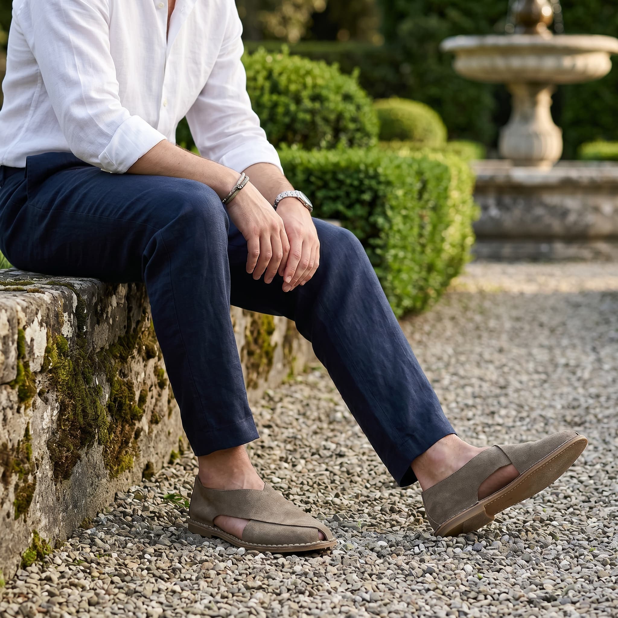 Person sitting on a stone wall in a garden wearing brown shoes.