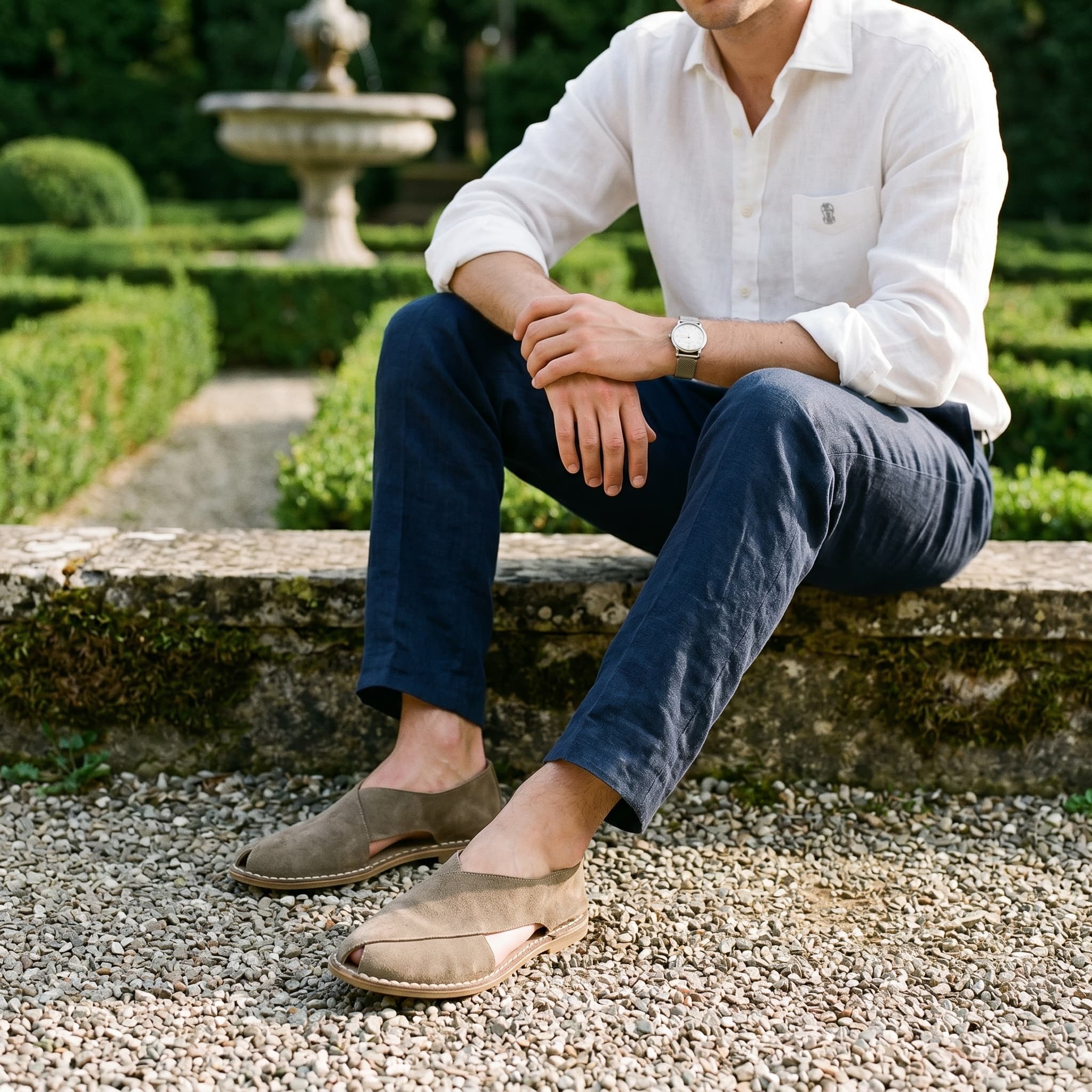 Man sitting outdoors in a garden wearing a white shirt and dark pants.