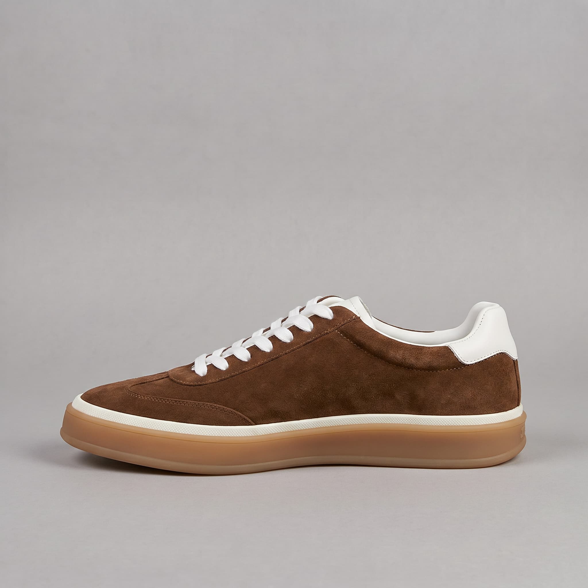Brown suede sneaker with white laces on a gray background