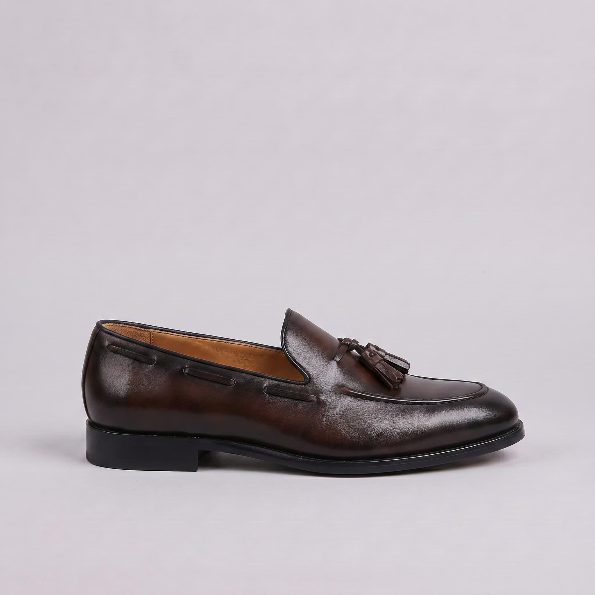 Brown leather loafer with tassel on a light gray background