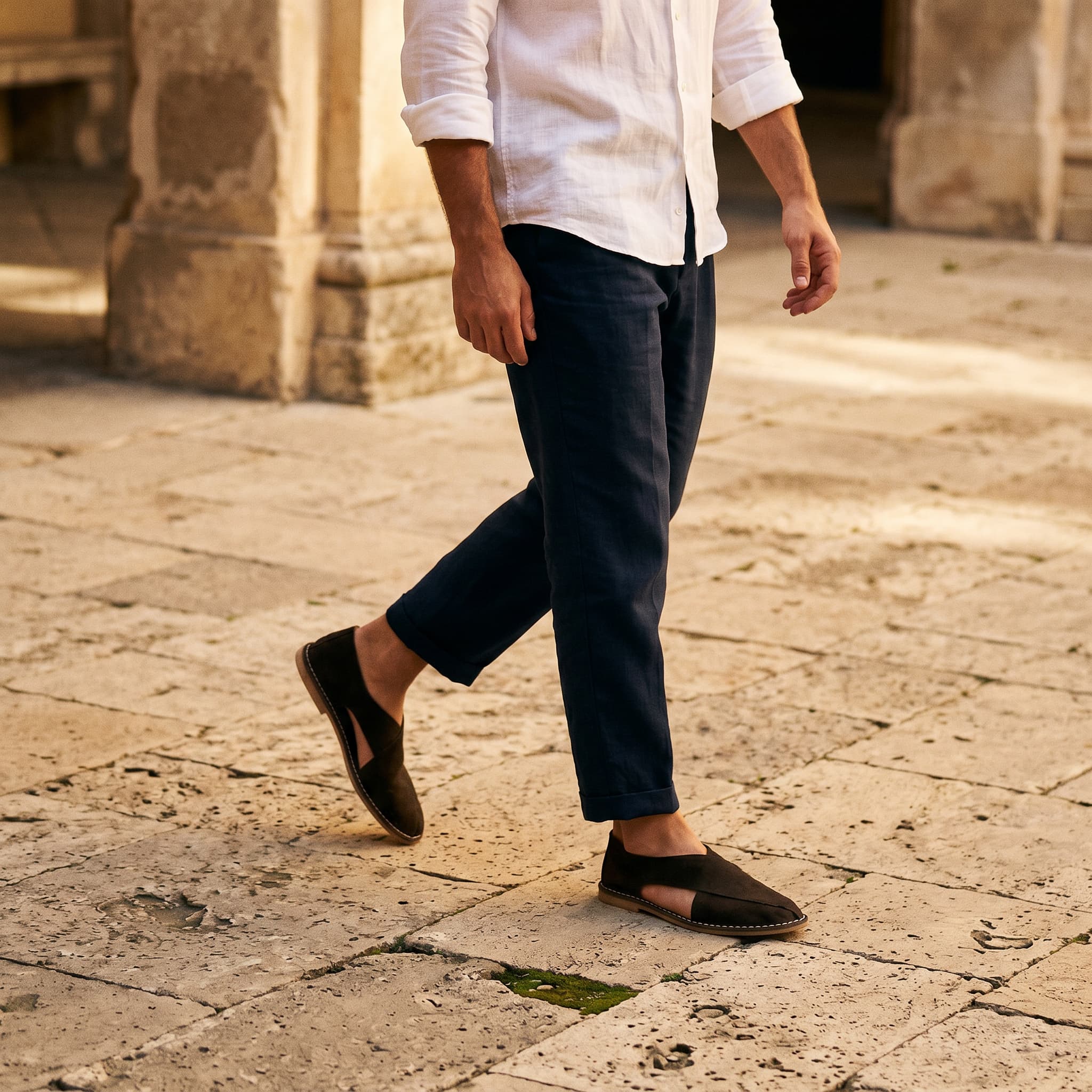 Person wearing a white shirt and dark pants walking on a stone pavement.